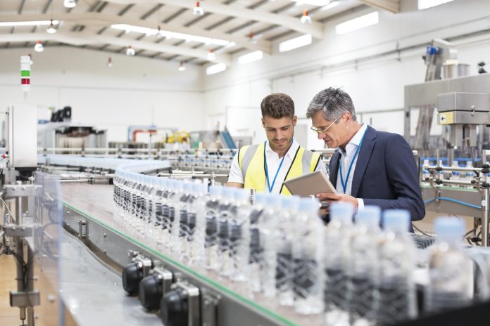 Supervisor and manager watching plastic bottles on conveyor belt