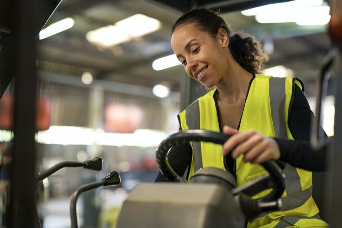 Smiling of Female warehouse controller driving a forklift in factory warehouse.